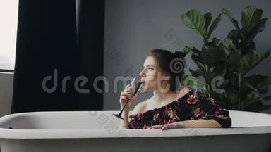迷人的年轻女子喝着香槟，<strong>辛苦</strong>工作一天后在浴缸里放松。 有魅力的女人喝香槟